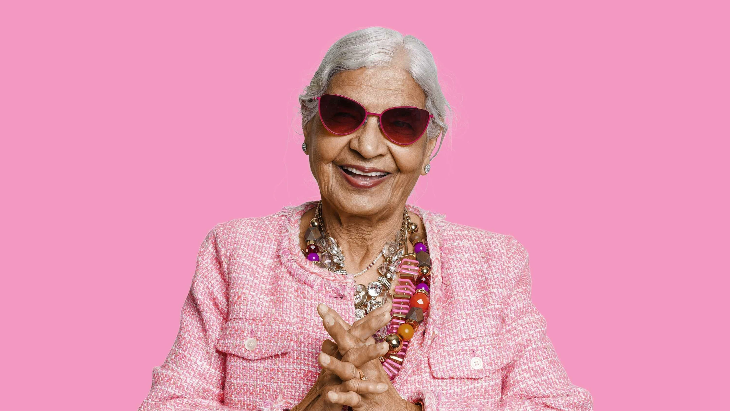 Old woman with pink jacket and matching sunglasses on a pink background