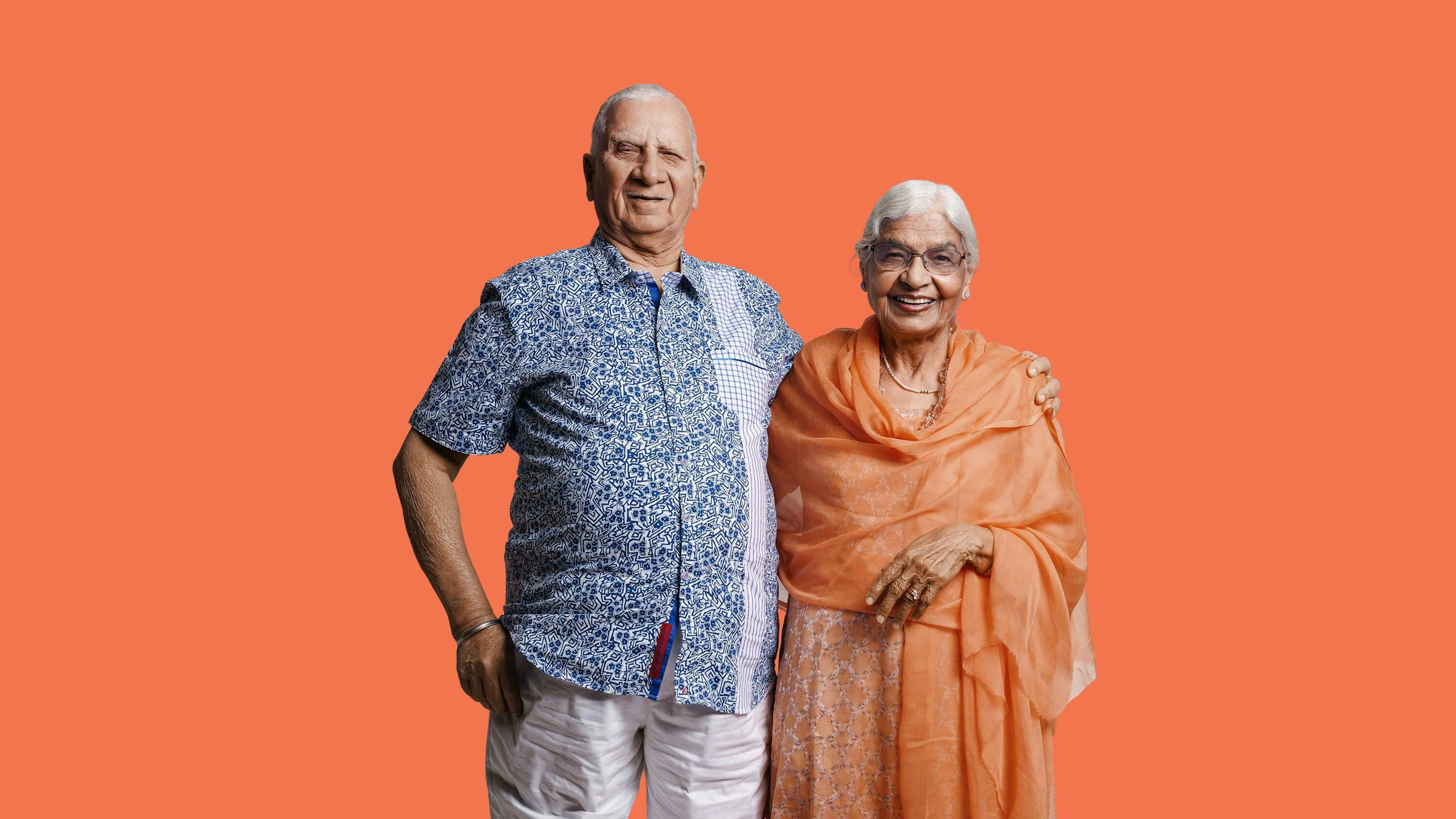 Elderly couple embracing and smiling on orange background