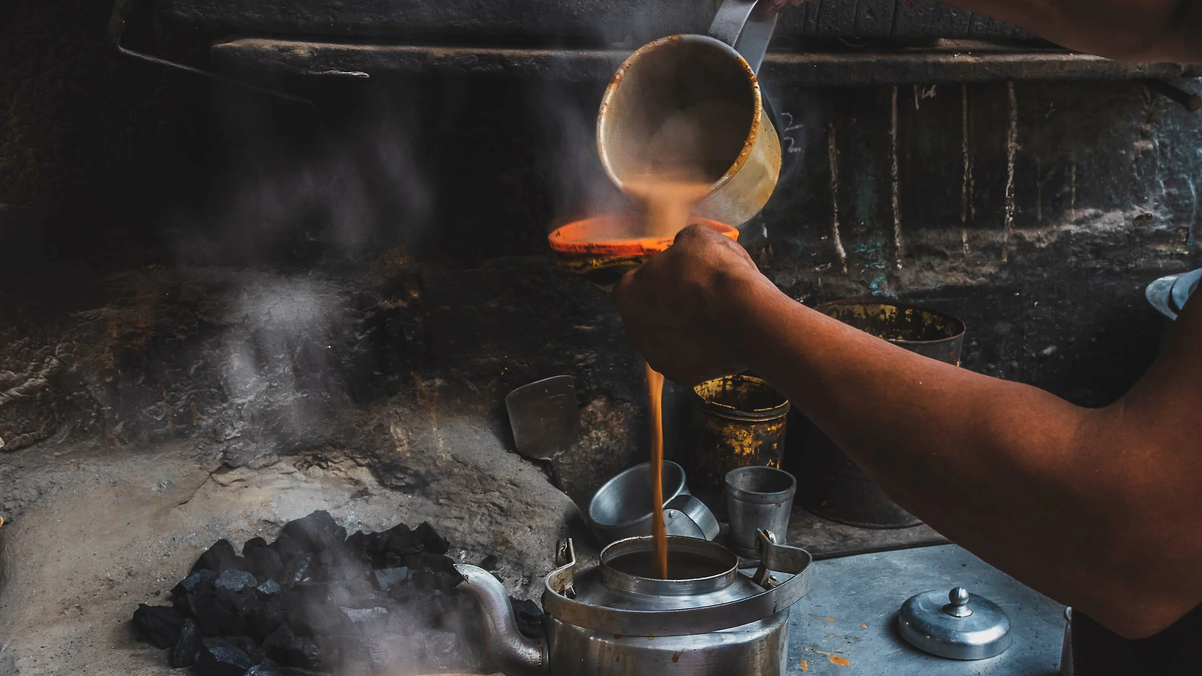 Hot chai being poured through an orange strainer into a metal canteen.